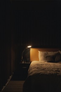 A dark bedroom with bed lit by a single light
