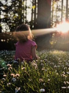 Little girl sits in grass enjoying the Sunset