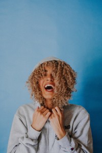 Curly haired woman stands laughing in a hoodie